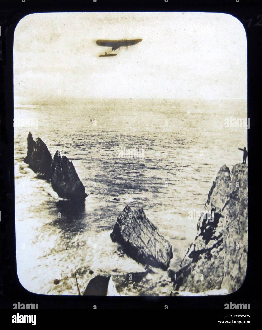 Une diapositive magique représentant l'aviateur français Léon Morane dans son monoplan Bleriot pendant son vol vers le phare Needles, à une distance de 21 miles en 25 minutes. Ce fut fait le 17 juillet 1910 lors de son apparition au Bournemouth Air Show. Diapositive publiée par W. Butcher & Sons, Londres et datant d'environ 1914. Banque D'Images