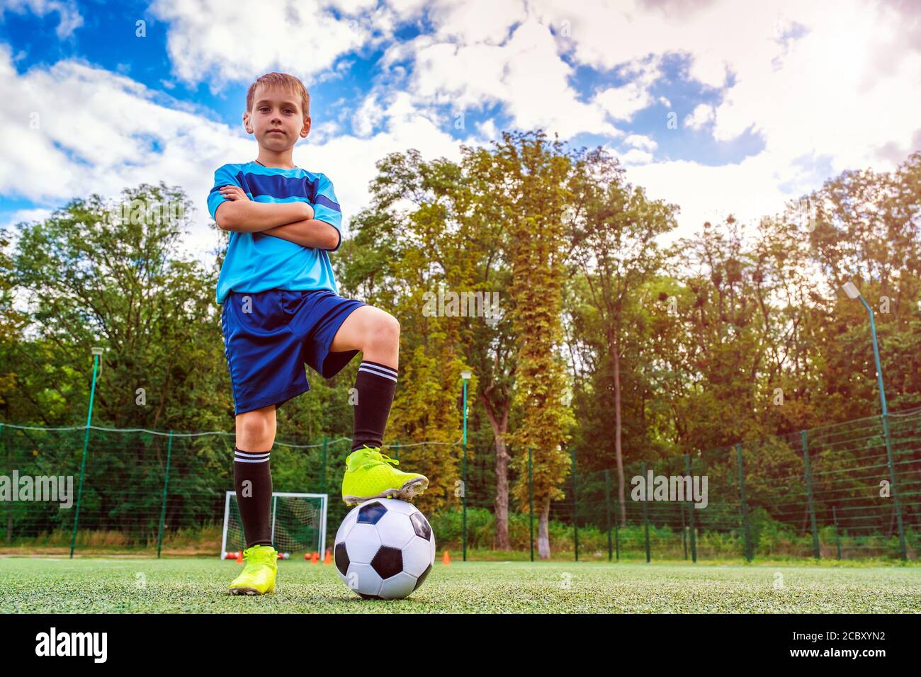 Portrait complet d'un enfant en vêtements de sport posé avec un ballon de football à l'extérieur Banque D'Images