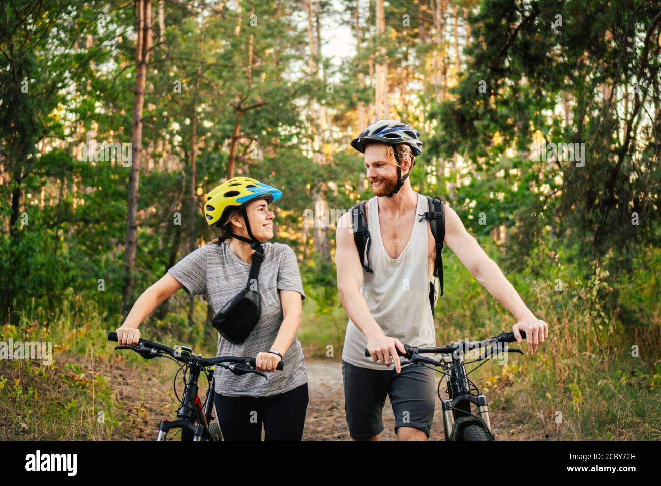 Couple joyeux poussant des vélos et marchant le long de la route de la forêt. Couple heureux avec vélo de marche dans le parc et de parler et rire. Caucasien Banque D'Images