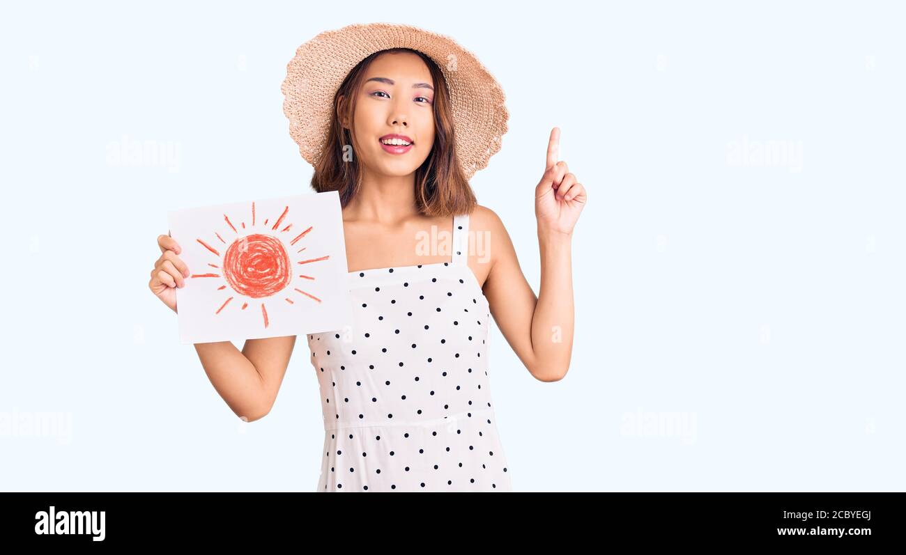 Jeune belle fille chinoise portant un chapeau d'été tenant le soleil  dessiner surpris par une idée ou une question pointant du doigt avec le  visage heureux, numéro un Photo Stock - Alamy