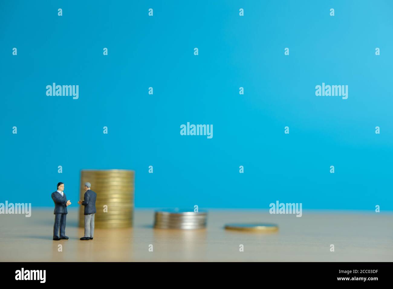 Concept d'affaires miniature - deux hommes d'affaires font une poignée de main pour poignée de main de l'accord de partenariat devant la pile de pièces Banque D'Images