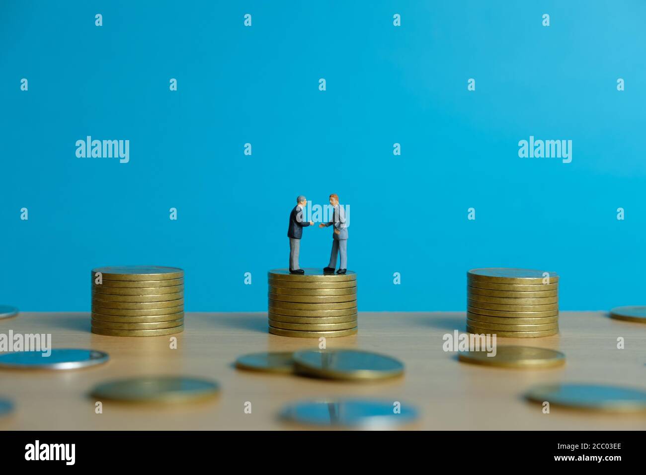 Concept d'affaires miniature - deux hommes d'affaires font une poignée de main pour poignée de main de l'accord de partenariat au-dessus de la pile de pièces Banque D'Images