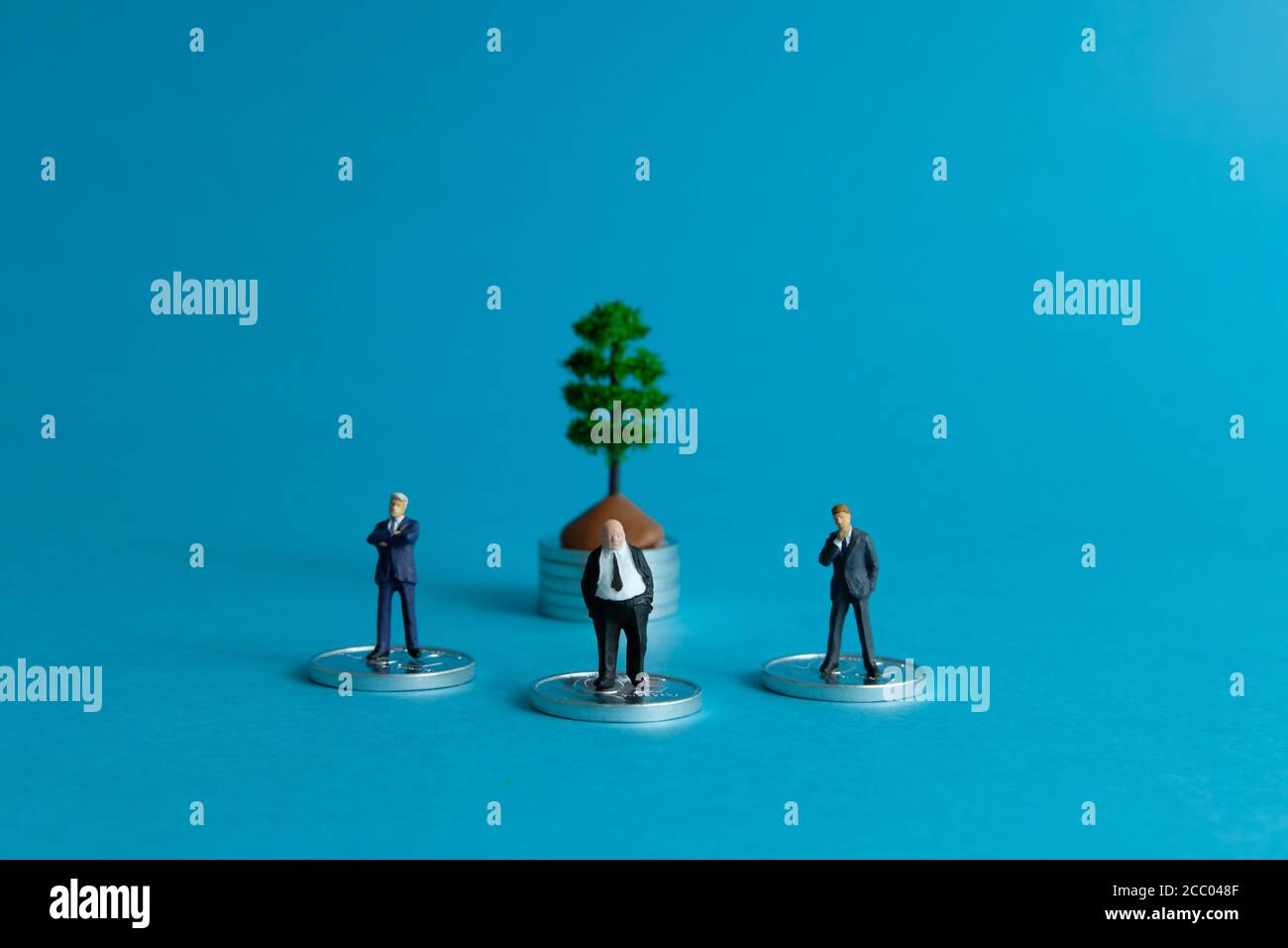 Concept d'entreprise miniature - trois hommes d'affaires debout devant pile de pièces de monnaie pensant à l'investissement financier Banque D'Images