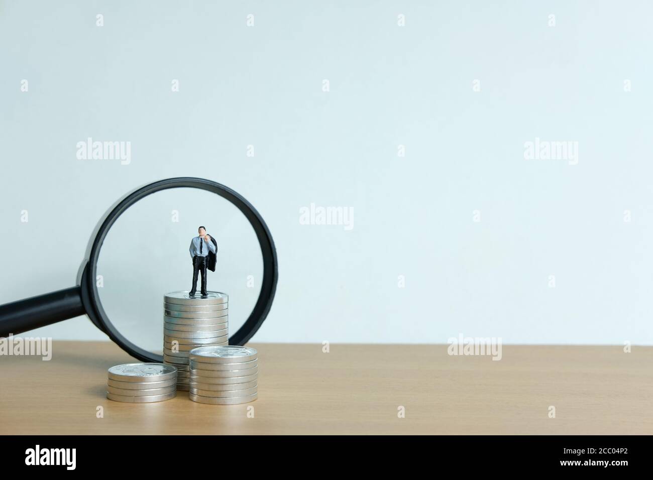 Miniature People concept - un homme d'affaires debout sur la pile de pièces avec loupe Banque D'Images