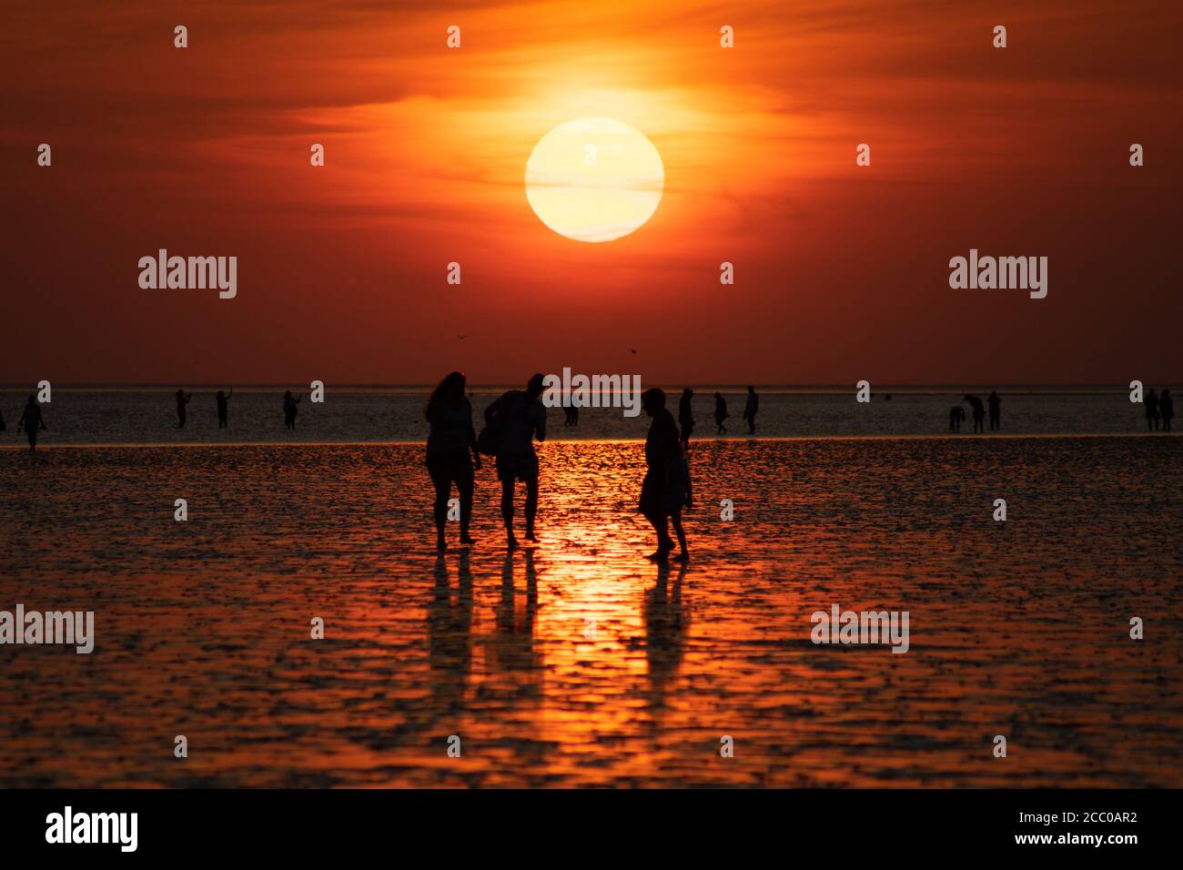 Un groupe de personnes sur la plage dans la réflektion du coucher de soleil au large de Buesum dans la mer des Wadden. Une scène d'été. Banque D'Images