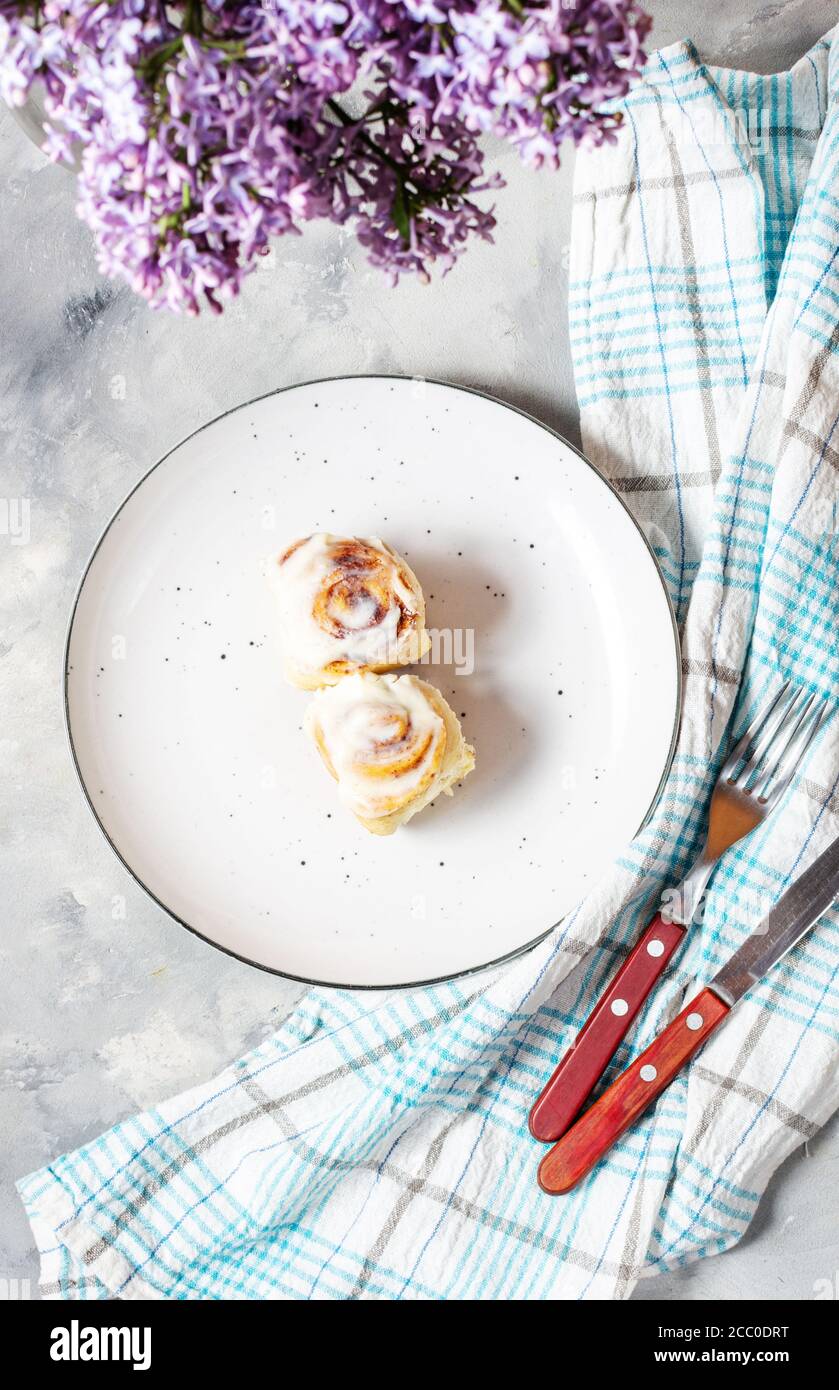 Roulé à la cannelle ou cinnabon avec glaçure de crème blanche sur plaque sur fond de béton. Brioches maison traditionnelles. Vue de dessus Banque D'Images