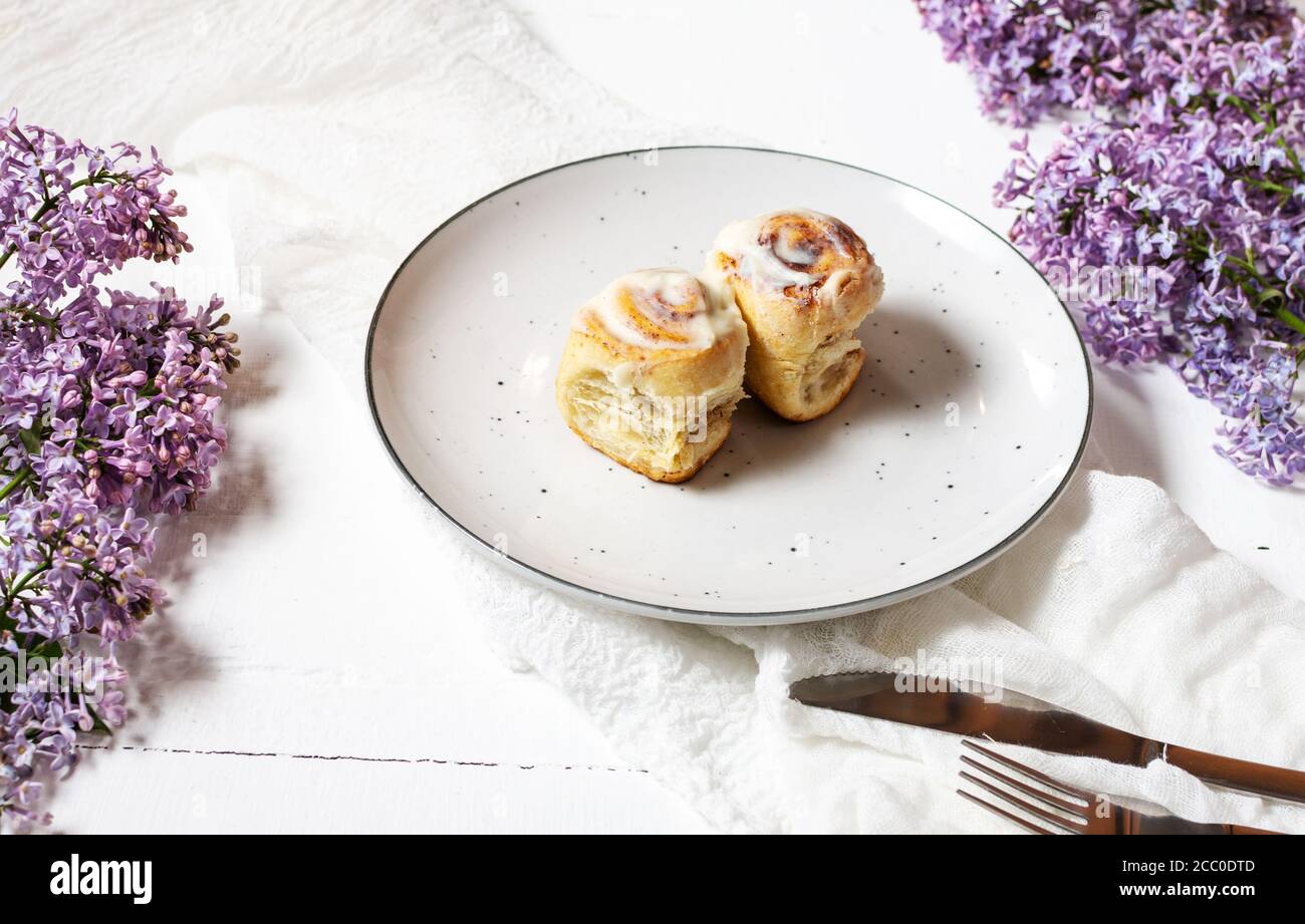 Roulé à la cannelle ou cinnabon avec glaçure de crème blanche sur plaque sur fond de bois blanc. Brioches maison traditionnelles Banque D'Images