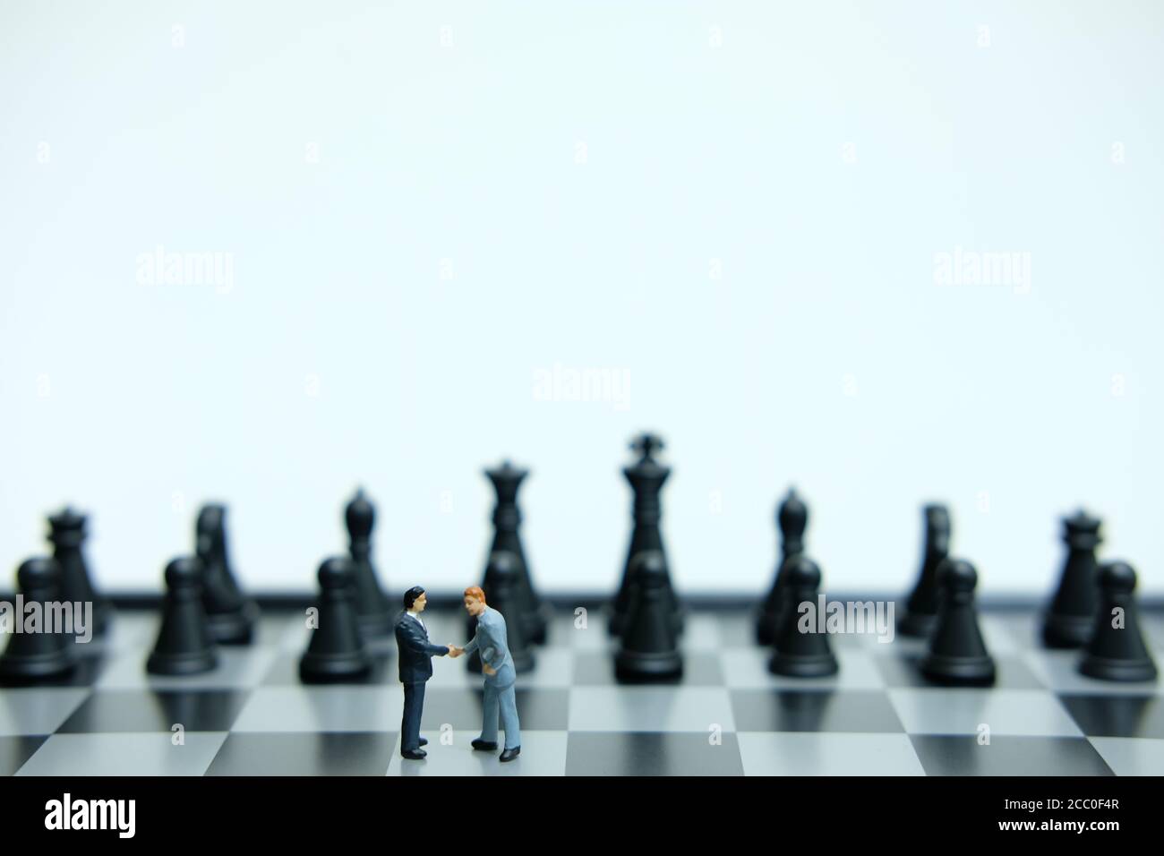 Concept d'entreprise miniature - deux hommes d'affaires font un accord de poignée de main avant du pion d'échecs Banque D'Images