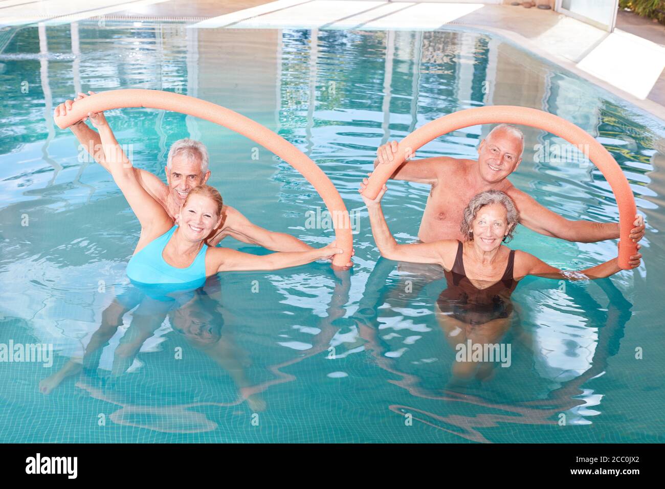 Le groupe senior fait de l'aqua fitness comme entraînement de dos avec la natation nouilles dans la piscine Banque D'Images