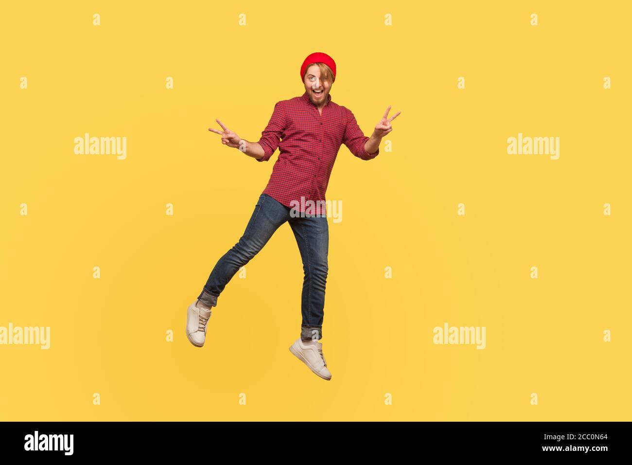 Portrait Joyeux hippster tendance mec en train de léviter, regardant l'appareil photo avec un geste de la paix de la victoire, planant en plein air, souriant et volant. Pleine longueur, Banque D'Images