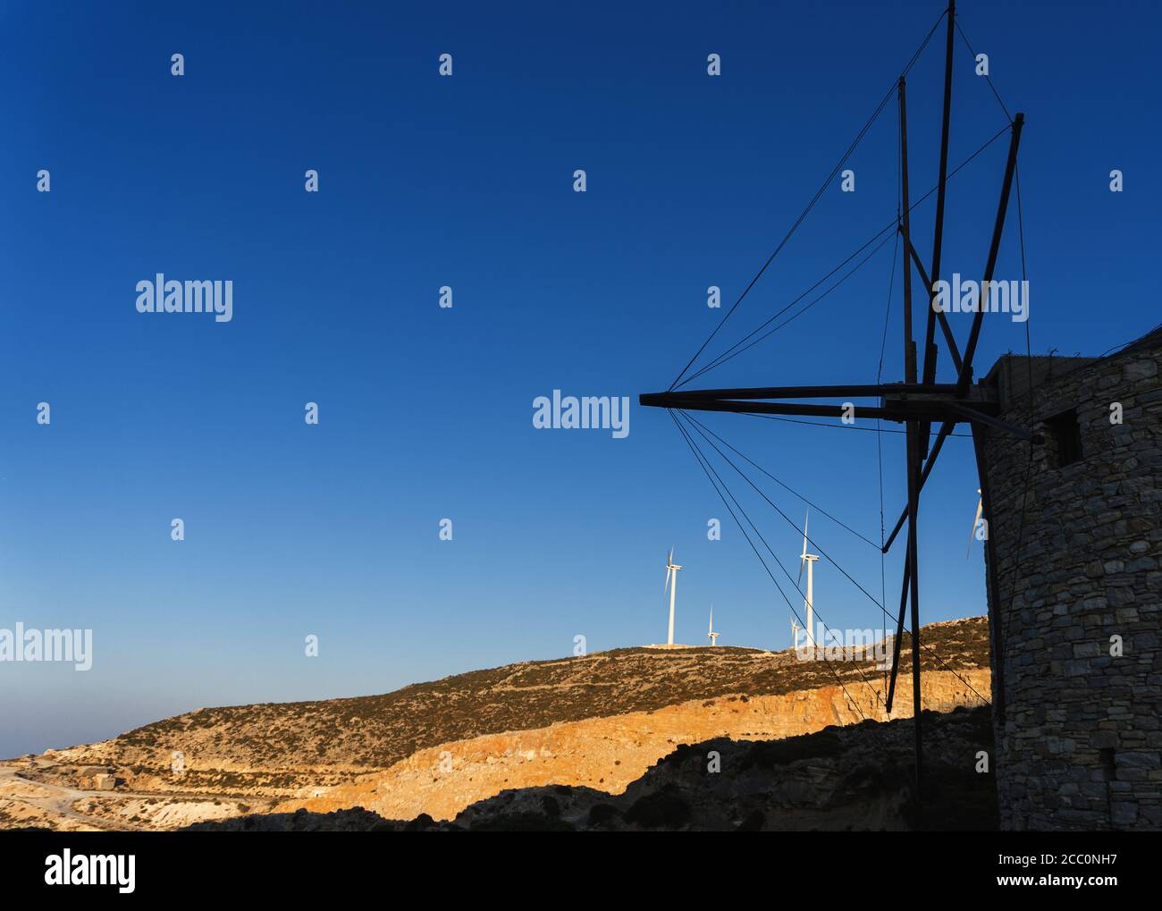 Un ancien moulin à vent sur fond d'éoliennes modernes sur une île grecque. Paysage vallonné éclairé par le soleil Banque D'Images