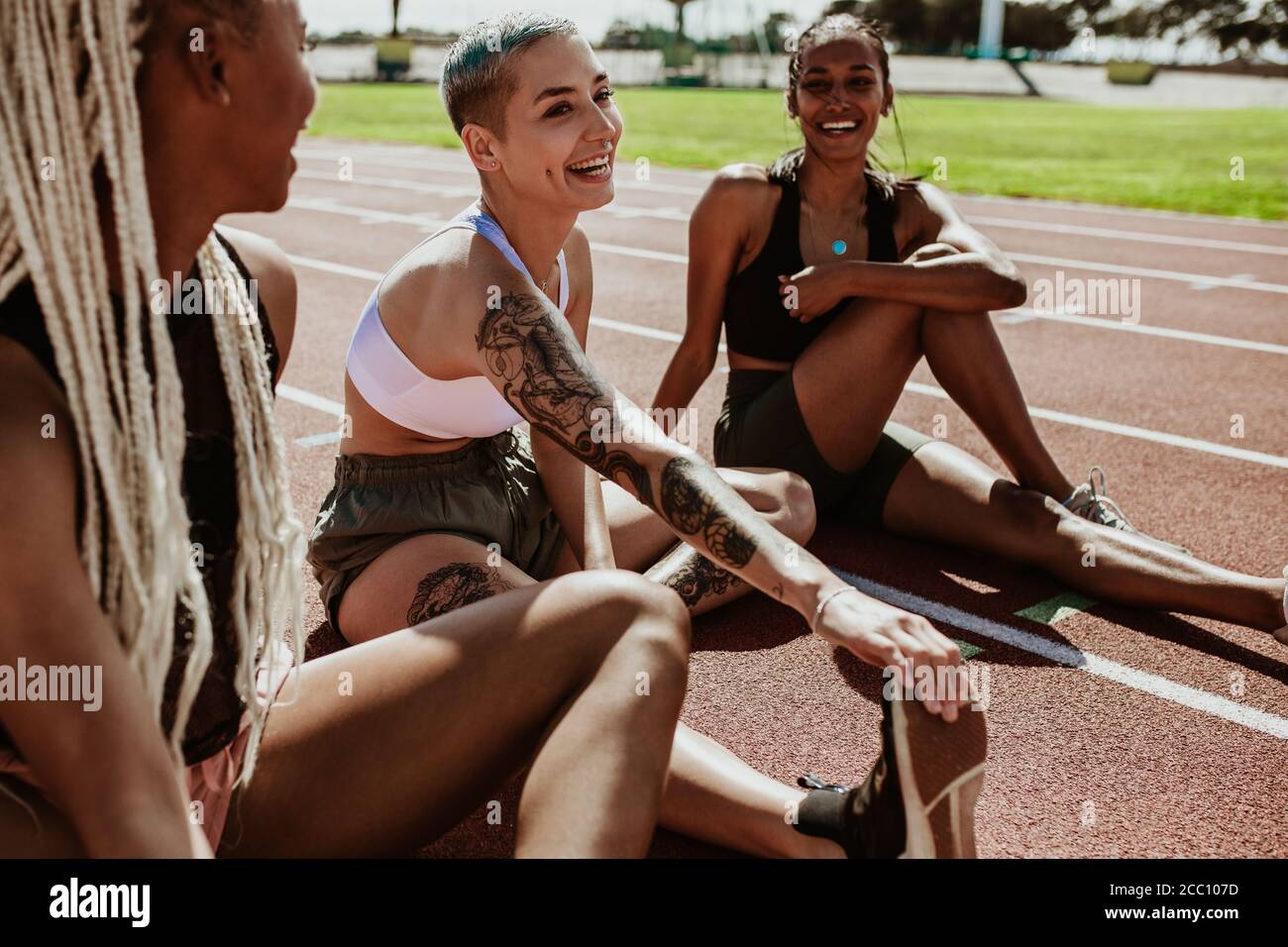 Groupe de trois coureuses prenant une pause après l'entraînement de course et étirant leurs jambes sur la piste de course. Les athlètes se détendent après un entraînement à Banque D'Images