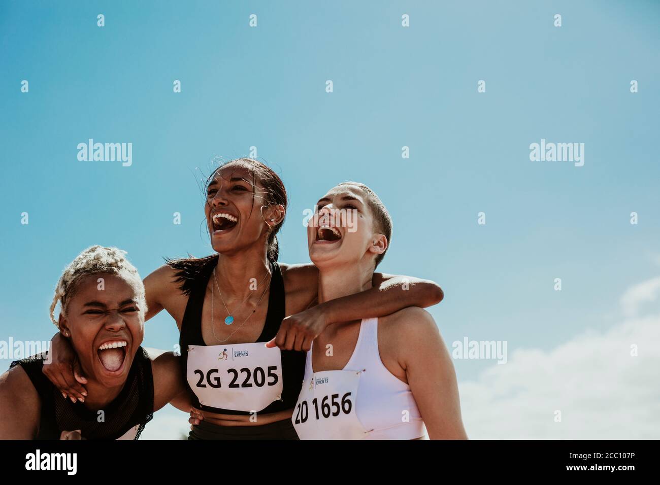 Une jeune équipe d'athlètes féminins debout ensemble et criant dans l'excitation. Groupe de coureurs divers profitant de la victoire. Banque D'Images