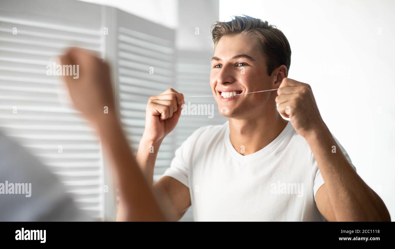 Beau jeune gars utilisant la soie dentaire dans la salle de bains Banque D'Images