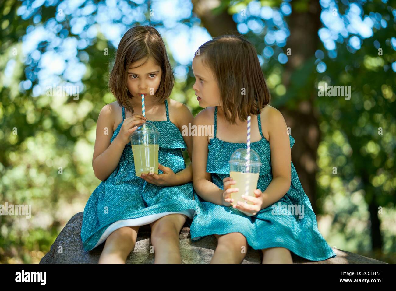 deux jolies petites filles en robe s'assoient sur une pierre et buvez de la limonade Banque D'Images