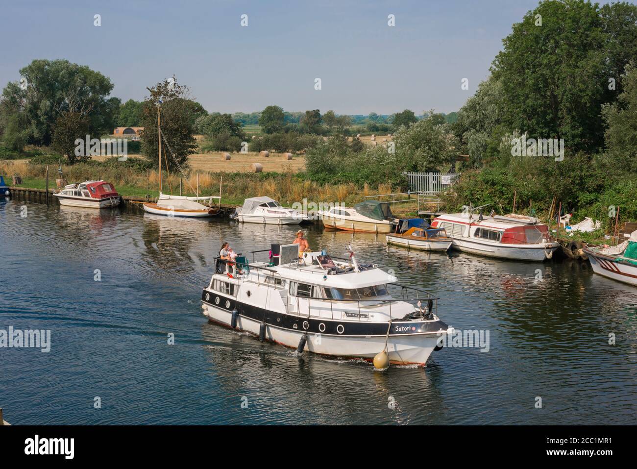 Vacances en bateau, vue en été d'un bateau de plaisance naviguant sur la rivière Waveney avec des bateaux amarrés sur le côté Norfolk de la rivière, East Anglia, Royaume-Uni Banque D'Images