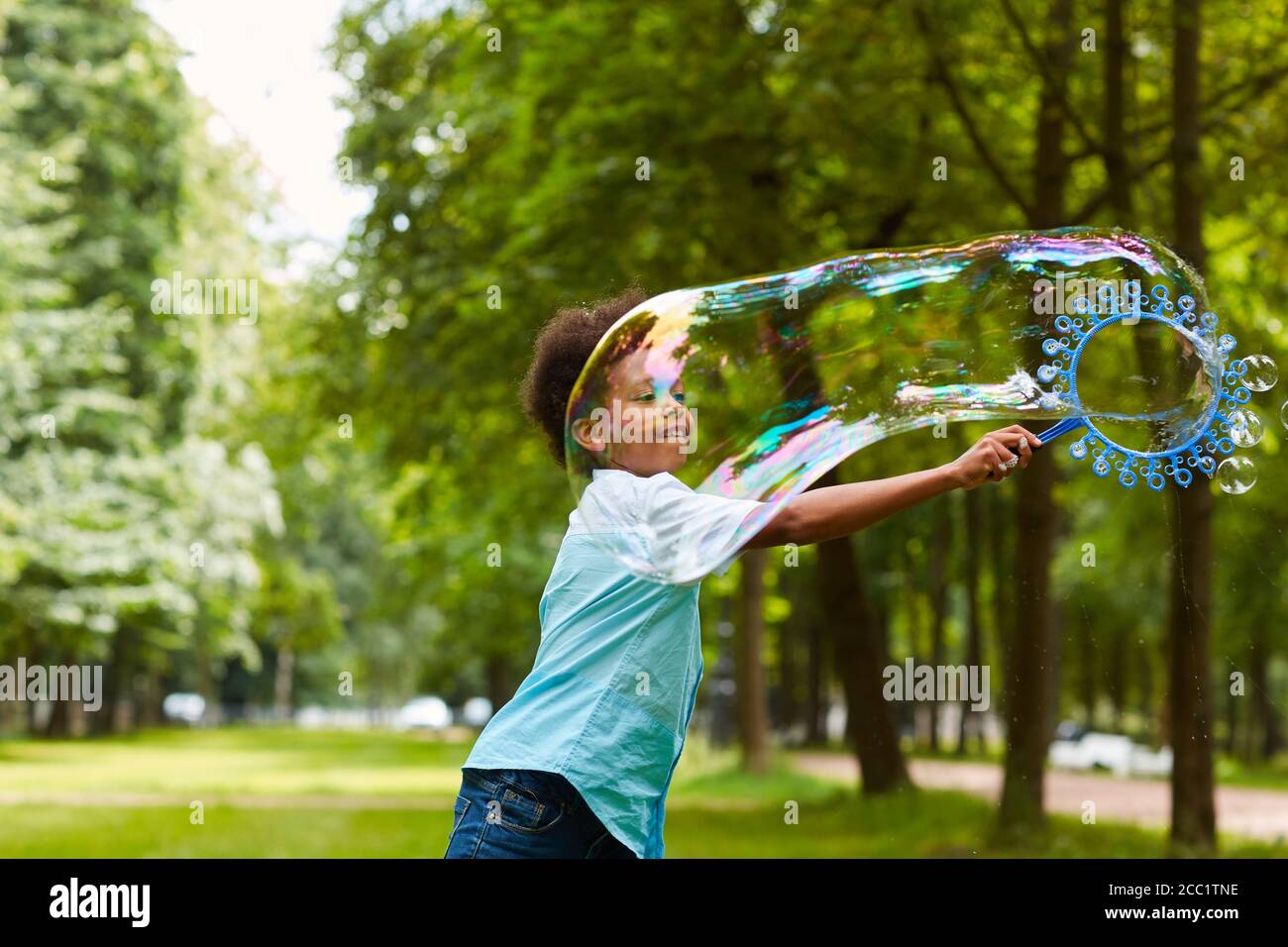 Portrait à la taille du mignon garçon afro-américain jouant avec des bulles à l'extérieur dans le parc vert tenant une grande baguette à bulles, espace de copie Banque D'Images