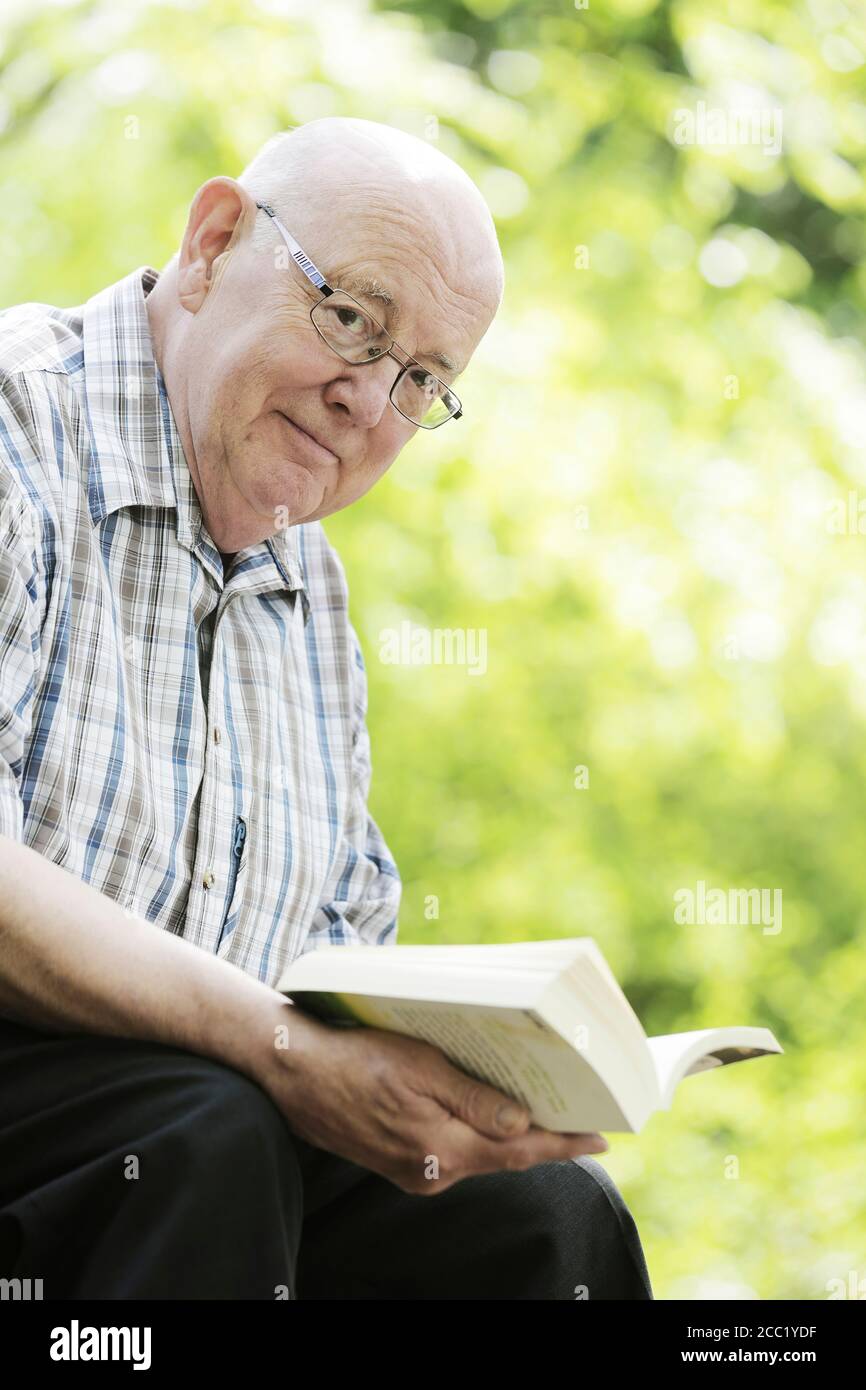 Allemagne, North Rhine Westphalia, Cologne, Portrait of senior man reading book on bench in park, smiling Banque D'Images