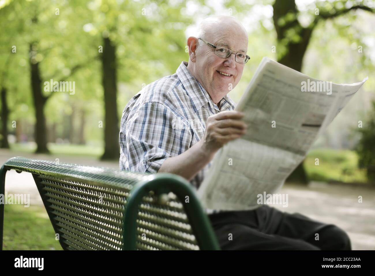 L'Allemagne, en Rhénanie du Nord-Westphalie, Cologne, Senior man reading newspaper on bench in park Banque D'Images