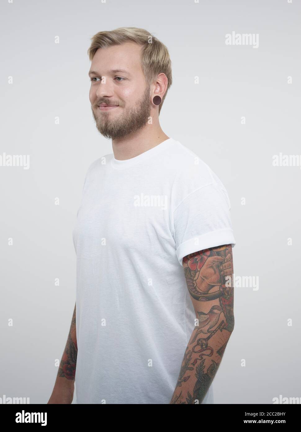 Jeune homme aux tatouages against white background, smiling Banque D'Images