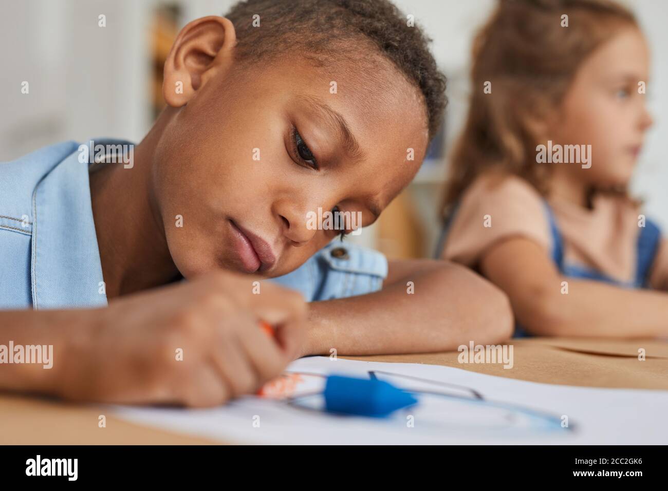 Gros plan portrait d'un garçon afro-américain en train de dessiner des images avec des crayons tout en appréciant la classe d'art dans le centre préscolaire ou de développement, l'espace de copie Banque D'Images