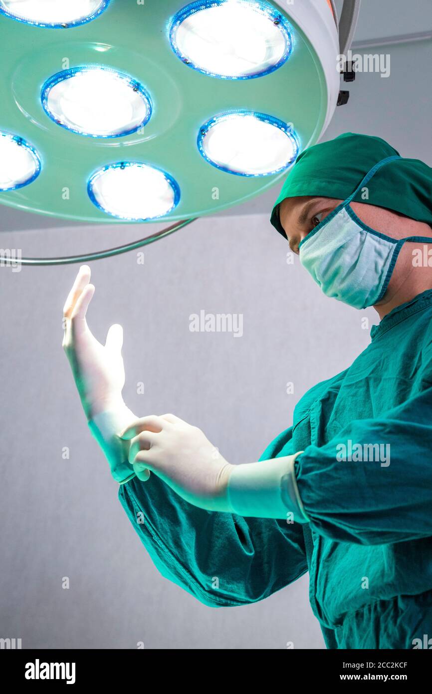 Chirurgien professionnel médecin préparant et portant des gants chirurgicaux sur les mains avant la chirurgie dans la salle d'opération des urgences de l'hôpital. Banque D'Images