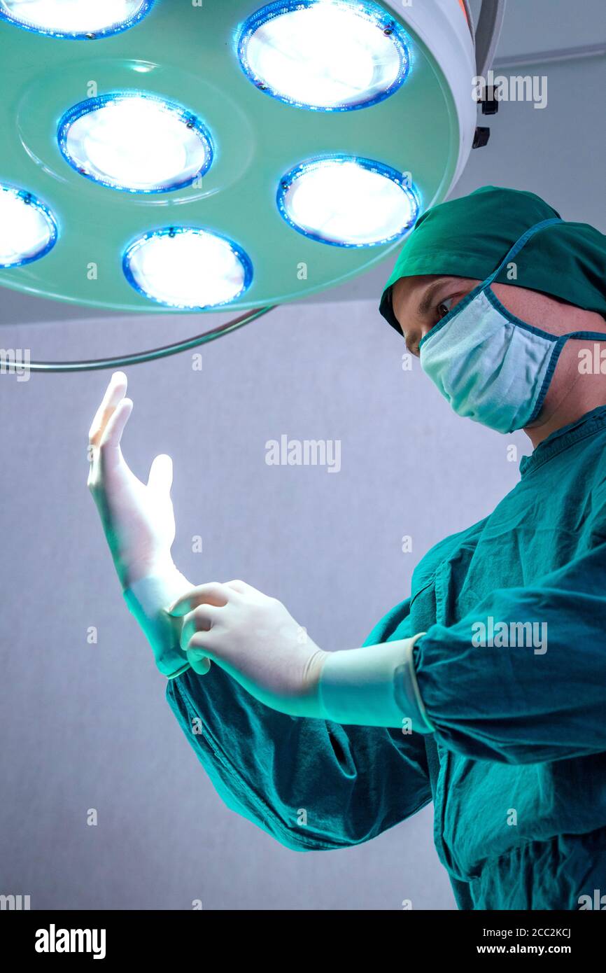 Chirurgien professionnel médecin préparant et portant des gants chirurgicaux sur les mains avant la chirurgie dans la salle d'opération des urgences de l'hôpital. Banque D'Images