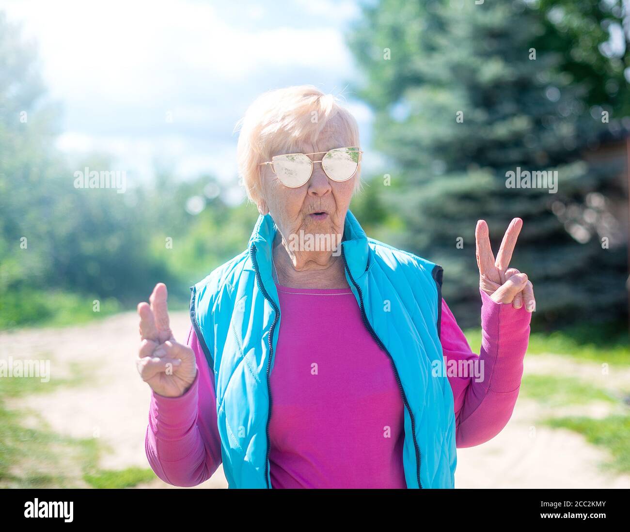 Une grand-mère de 90 ans à la mode et heureuse avec des cheveux gris, des lunettes de soleil et un sourire dans la nature, le temps d'un soleil d'été. Banque D'Images