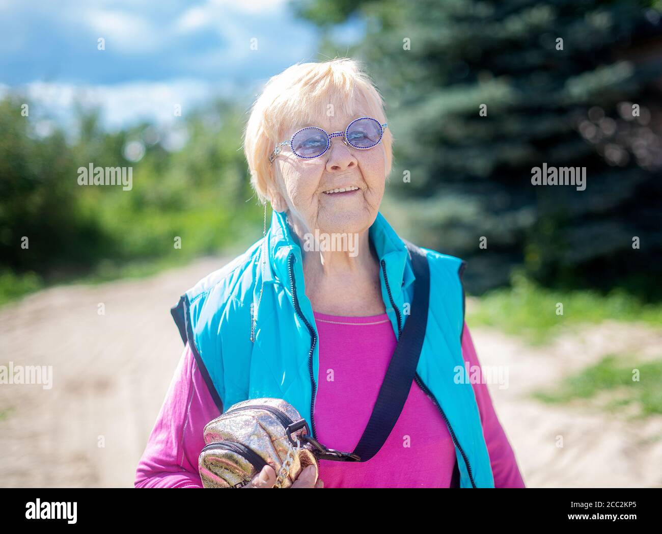 Une grand-mère de 90 ans heureuse et tendance avec des cheveux gris, des lunettes de soleil et un sourire dans la nature lors d'un soleil d'été. Banque D'Images