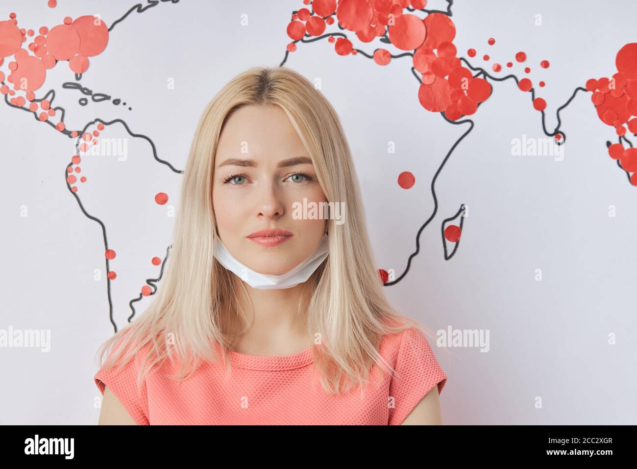 Portrait en gros plan de la triste femme caucasienne dans un masque de protection médicale pendant l'épidémie de Covid-19 dans le monde entier. Carte du monde avec des marques rouges de Coronav Banque D'Images