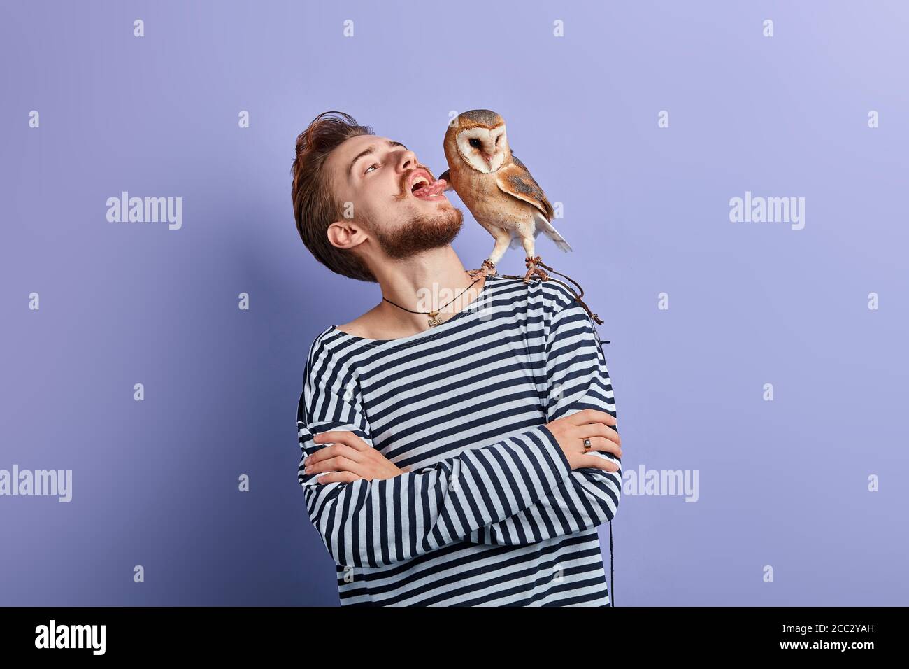 drôle d'homme fou avec les bras croisés mettant la langue, regardant la chouette, portrait de gros plan, isolé fond bleu .guy taquinant son oiseau Banque D'Images