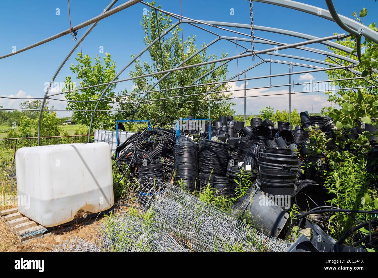 Réservoir de stockage en plastique avec insecticide liquide, clôture en treillis métallique et conteneurs en plastique noir dans la zone de stockage de l'exploitation commerciale de serre. Banque D'Images
