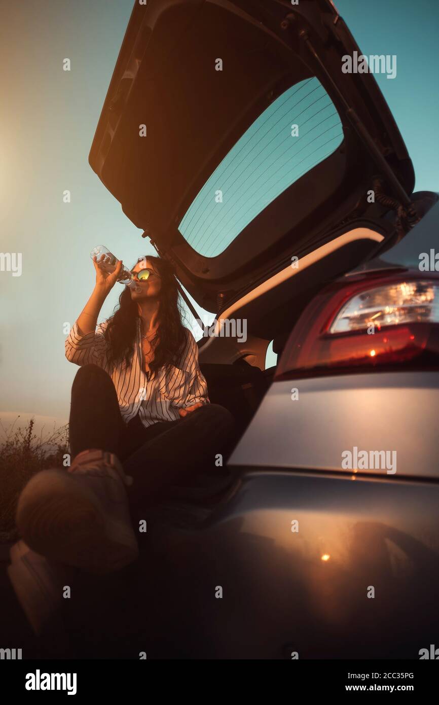 Belle jeune femme assise dans le coffre de voiture et de l'eau potable Banque D'Images