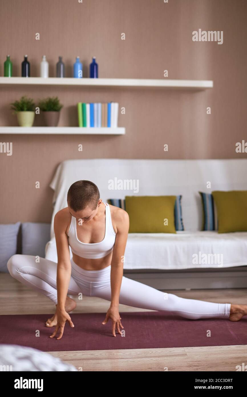 Jeune fille Slim faire les exercices de yoga à la maison. Vêtu de blanc et leggins sujet, la pratique des étirements. Garder les muscles de tonus Banque D'Images