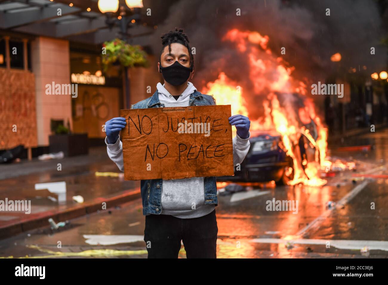 Seattle, USA 30 mai 2020 : tard dans la journée un activiste tenant un panneau NO JUSTICE NO PEACE alors qu'une voiture de police brûle en arrière-plan à Westlake. Banque D'Images