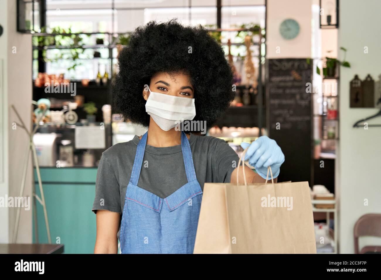 Femme africaine américaine de café travaillant avec un masque facial tenant un sac de nourriture à emporter. Banque D'Images Femme africaine américaine de café travaillant avec un masque facial tenant un sac de nourriture à emporter. Banque D'Images