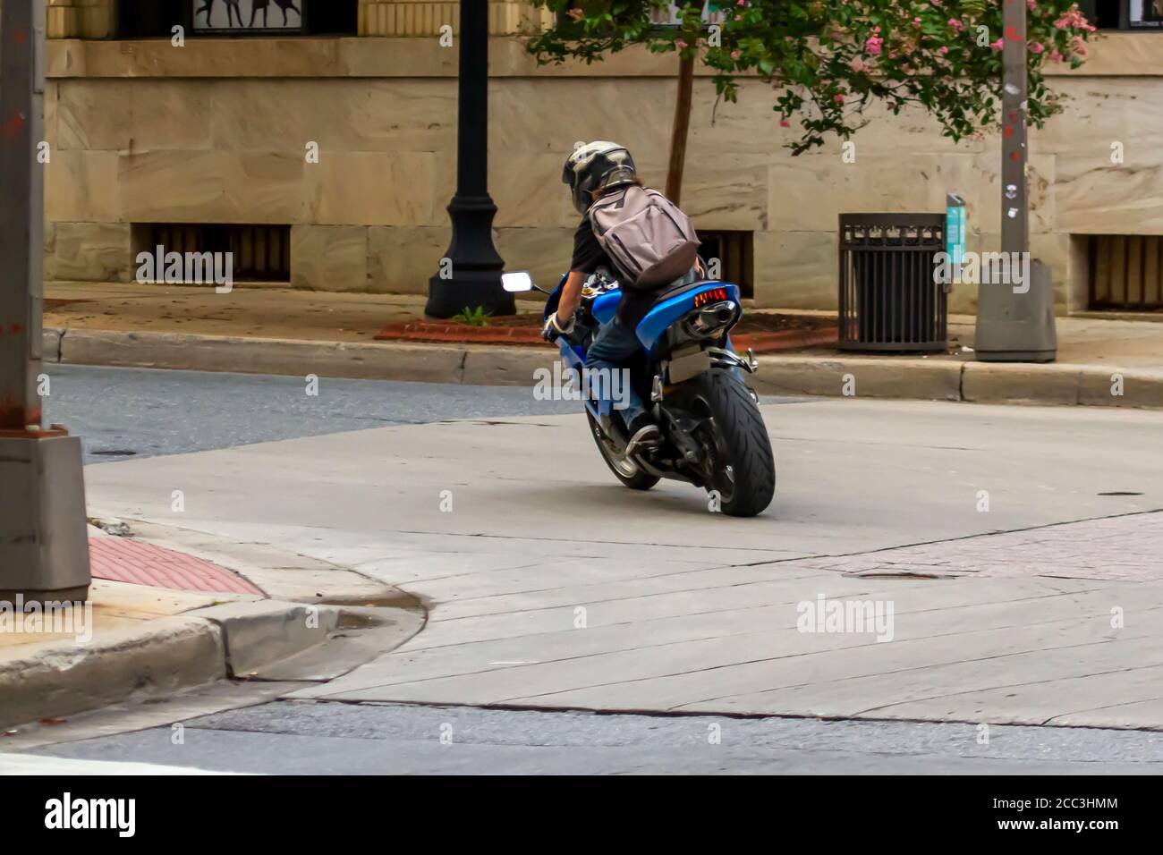 Un homme caucasien long aux cheveux portant un bakcpack, un t-shirt, des gants, un Jean et un casque est à cheval sur une moto sportive dans un endroit urbain. Fonctions d'image Banque D'Images