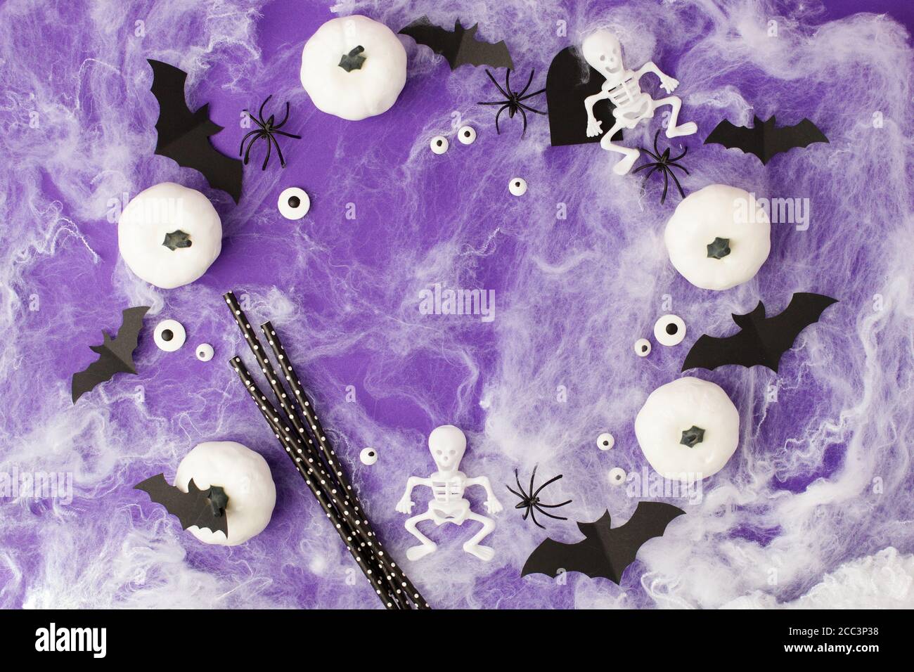 Décorations d'Halloween. Citrouilles blanches décoratives, chauves-souris, yeux, squelettes, pailles de crème pour cocktail sur fond violet. Concept de fête d'Halloween. FLA Banque D'Images