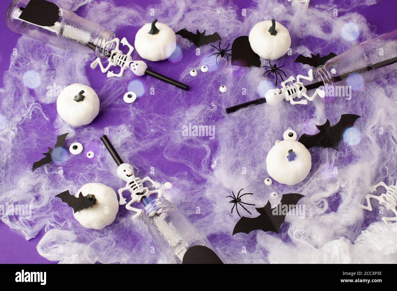 Joyeux Halloween concept de vacances. Décorations effrayantes, toile d'araignée, citrouilles, chauves-souris, bouteilles pour cocktails et pailles sur fond violet. Accueil de fête Banque D'Images