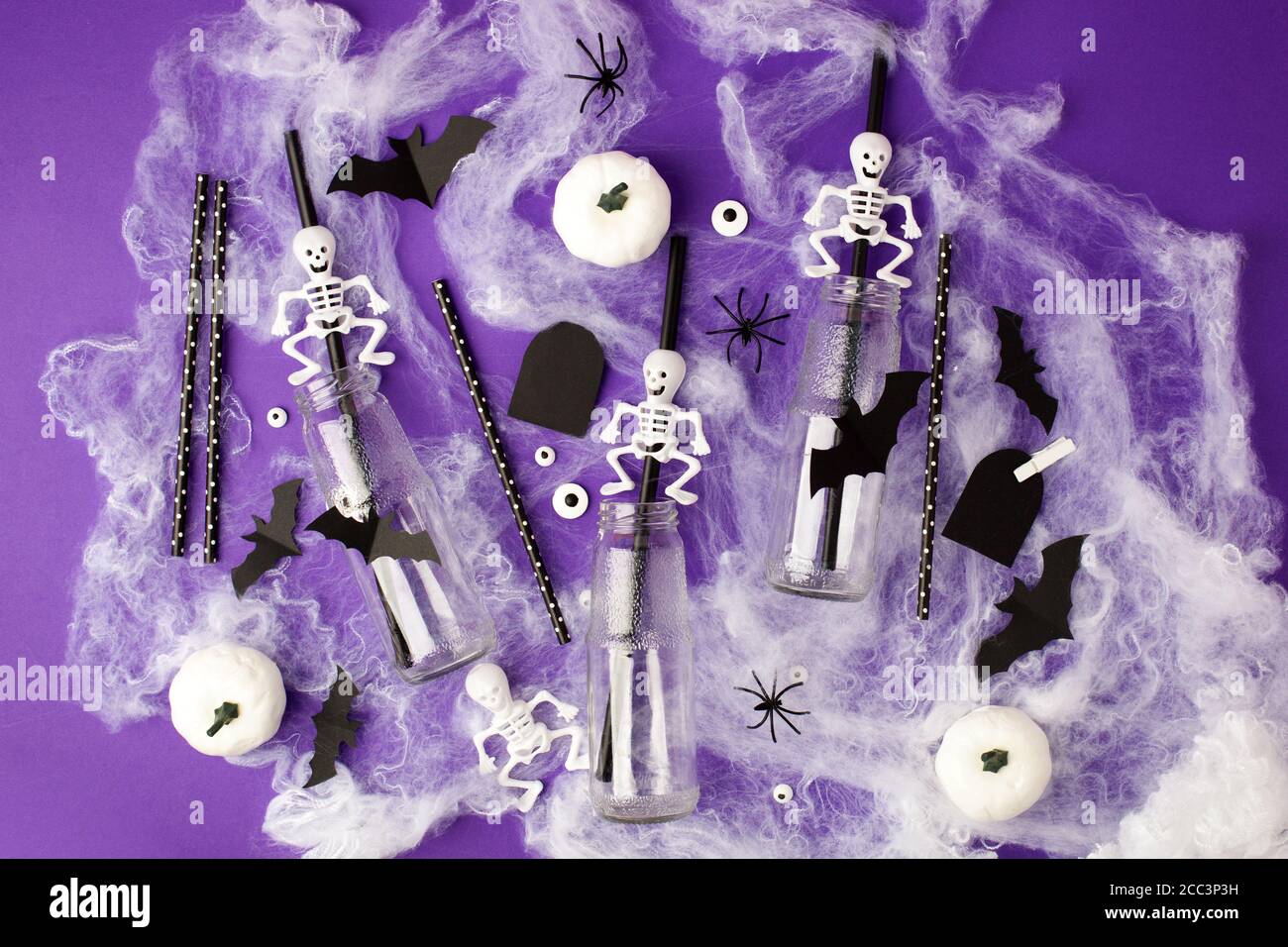 Joyeux Halloween concept de vacances. Décorations effrayantes, toile d'araignée, citrouilles, chauves-souris, bouteilles pour cocktails et pailles sur fond violet. Accueil de fête Banque D'Images