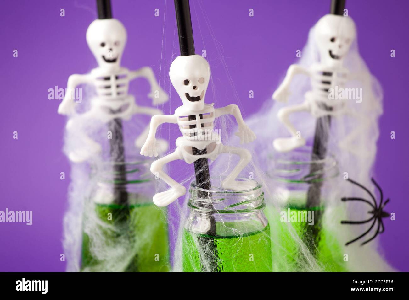 Composition Halloween avec boisson festive, cocktail vert toxique avec décor de fête effrayant squelette et araignées, toile d'araignée sur le backgroun violet traditionnel Banque D'Images