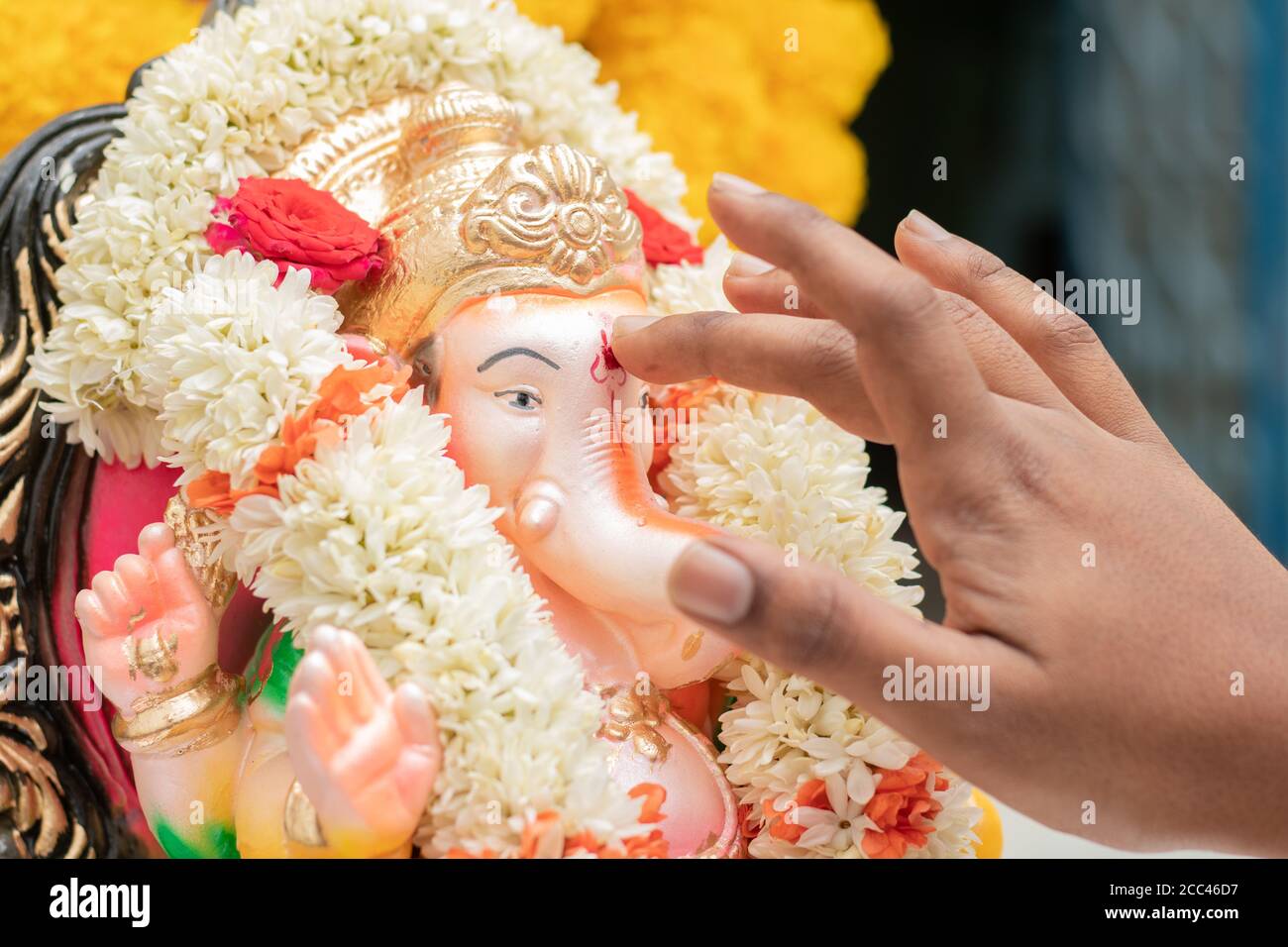 Gros plan des mains appliquant Tilak ou Kumkum au Seigneur Ganesha pendant la cérémonie religieuse indienne de ganesha ou de vinayaka Chaturthi festival. Banque D'Images