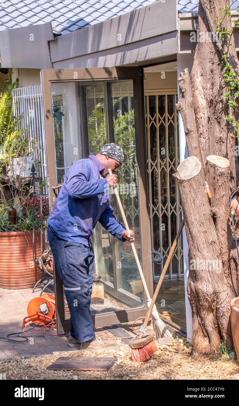 Alberton, Afrique du Sud - un travailleur migrant noir fait de la main-d'œuvre non qualifiée dans un jardin résidentiel pour gagner une image vivante en format vertical Banque D'Images