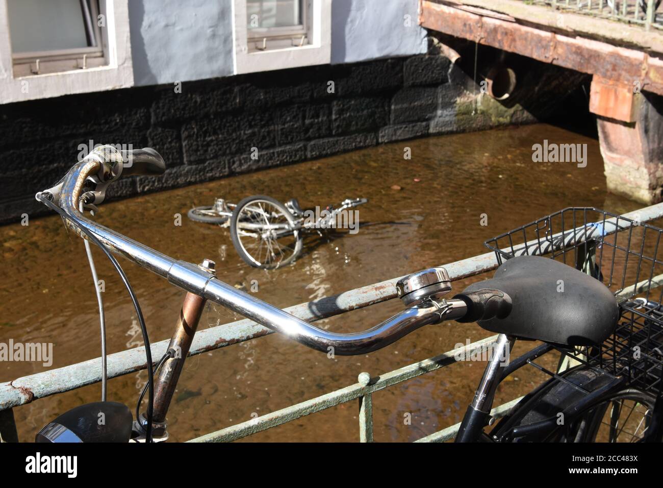 Vélo penché sur la rampe métallique du chenal d'eau de Fribourg. Dans l'eau courante est un squelette d'un vélo gravement endommagé ne plus convenable pour l'utilisation. Banque D'Images