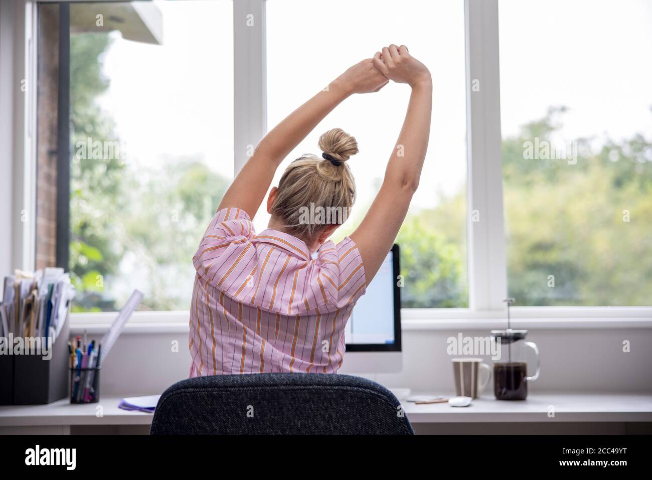 Vue arrière de la femme travaillant à domicile sur l'ordinateur dans Bureau à domicile s'étirant au bureau Banque D'Images