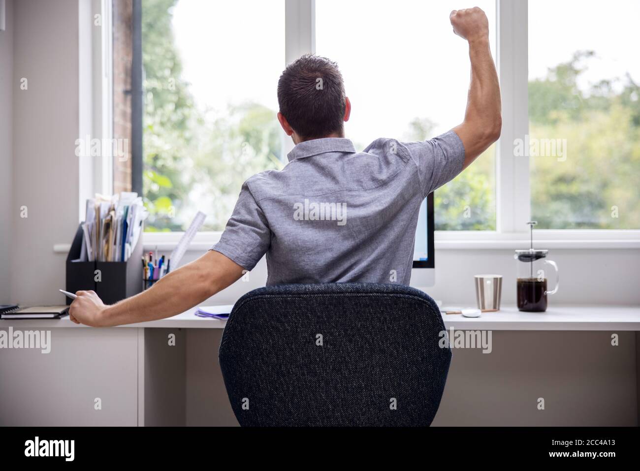 Vue arrière de l'homme travaillant à domicile sur l'ordinateur dans Bureau à domicile s'étirant au bureau Banque D'Images