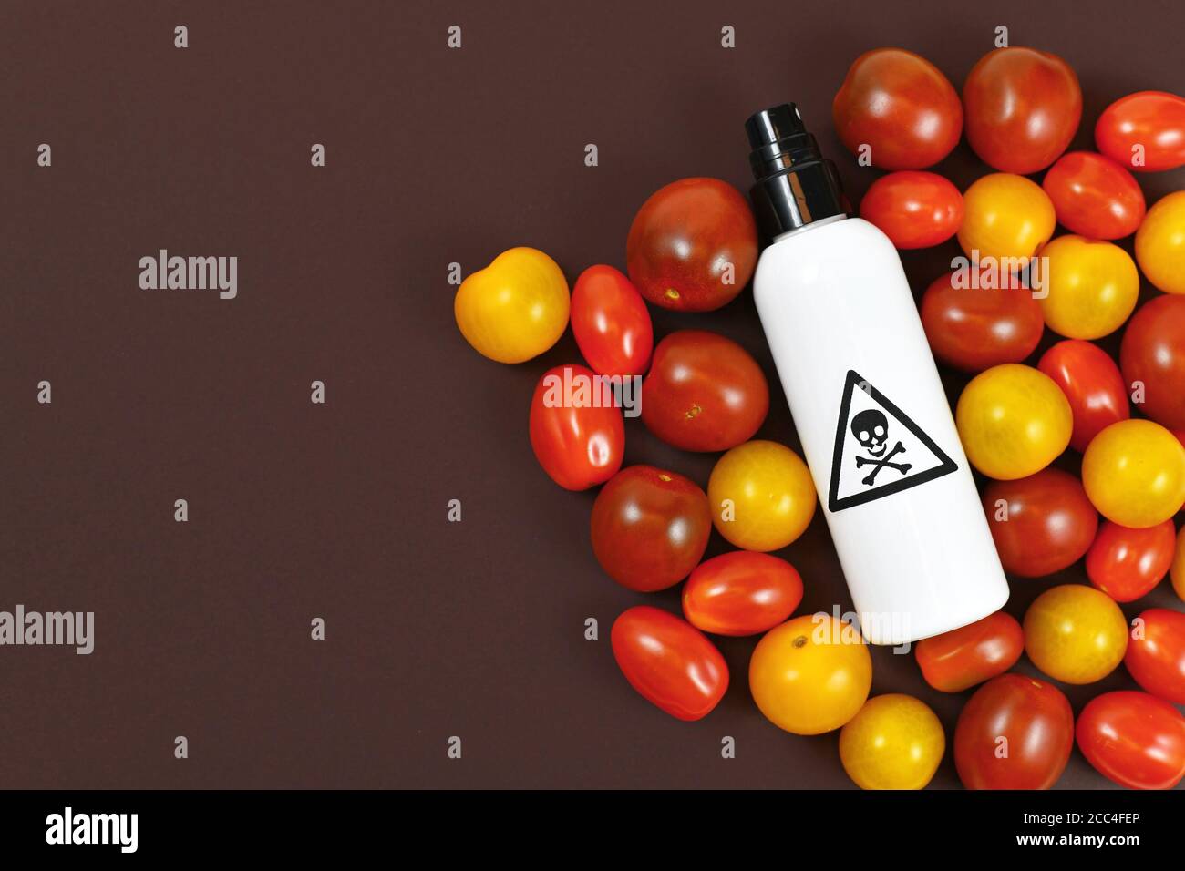 Concept d'utilisation de pesticides dangereux dans les produits alimentaires agricoles avec les tomates et vaporisez le flacon avec l'étiquette d'avertissement toxique avec crâne sur foncé Banque D'Images