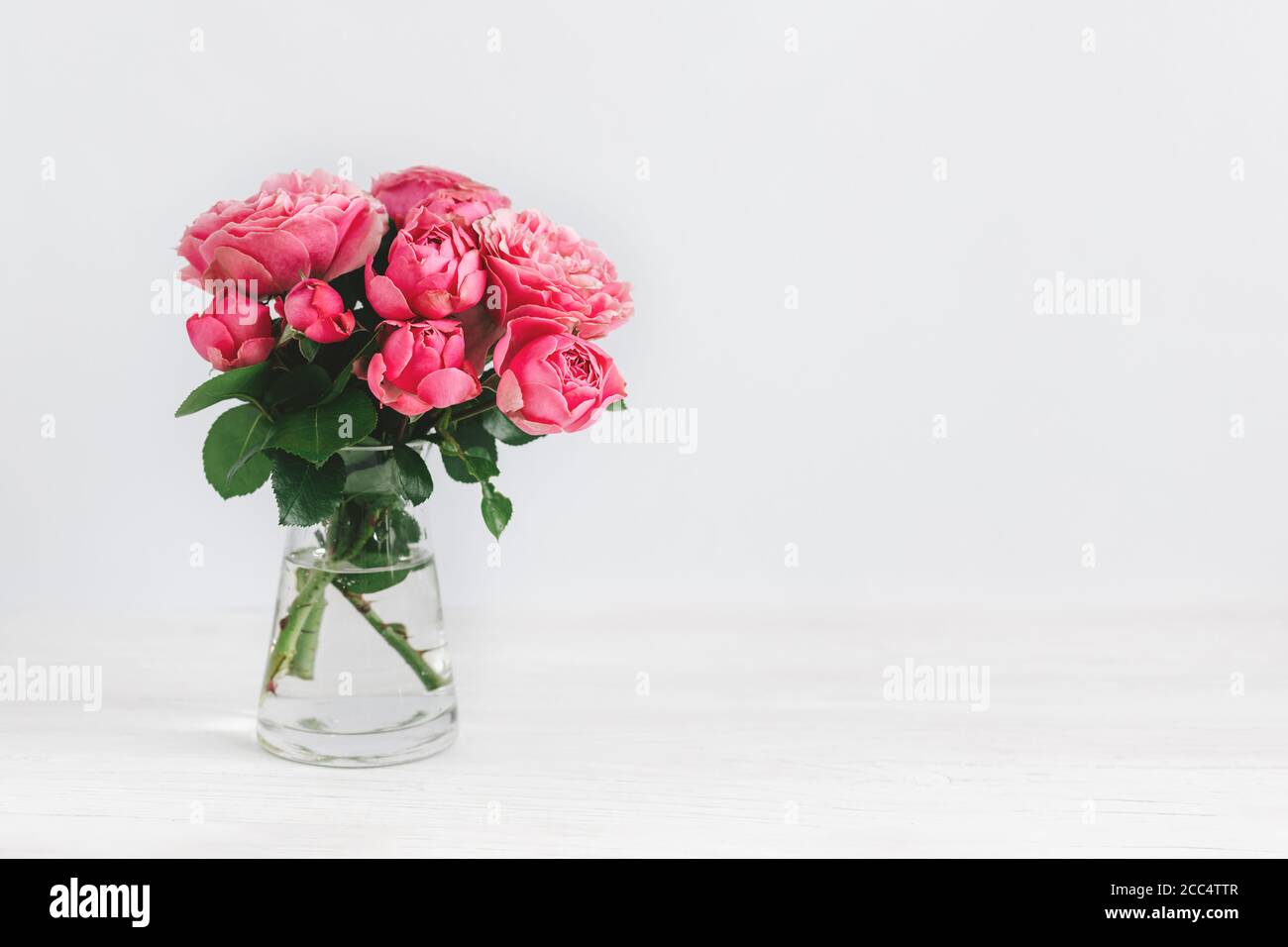 Bouquet romantique de roses roses dans un vase en verre sur fond blanc. Placer pour le texte. Banque D'Images