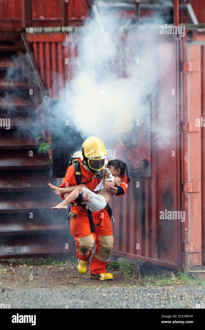 Le pompier a aidé la fille. Laissez le bâtiment brûlant et fumé. Banque D'Images