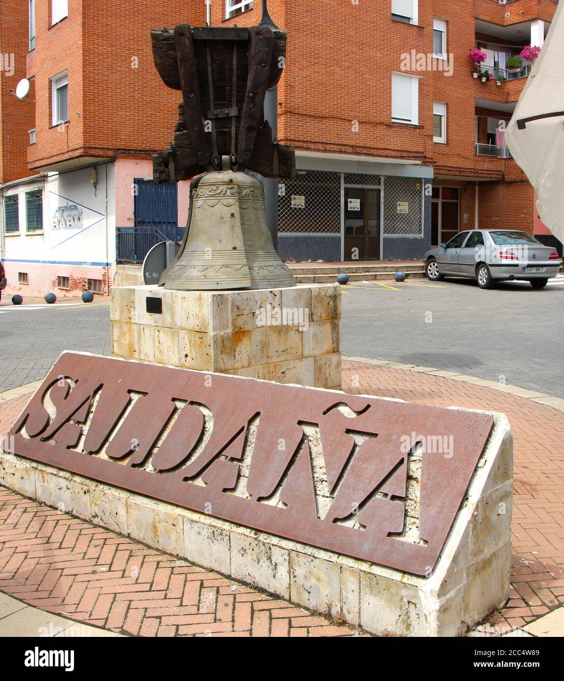Nom de la ville et ancienne cloche d'église avec hangar en bois exposé à Saldaña Palencia Espagne un jour nuageux d'août quand le marché est ouvert tous les mardis Banque D'Images